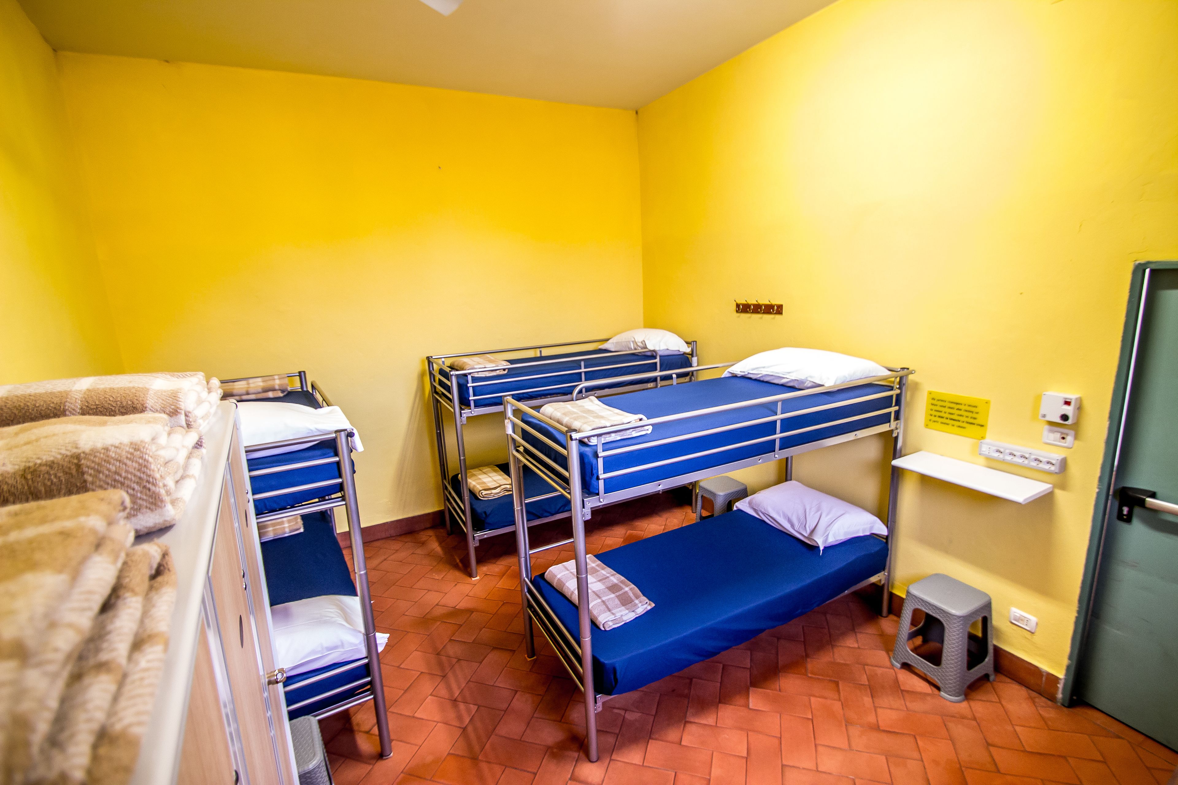 A dormitory room with bunk beds, a small stool, and a shelf with a sign.