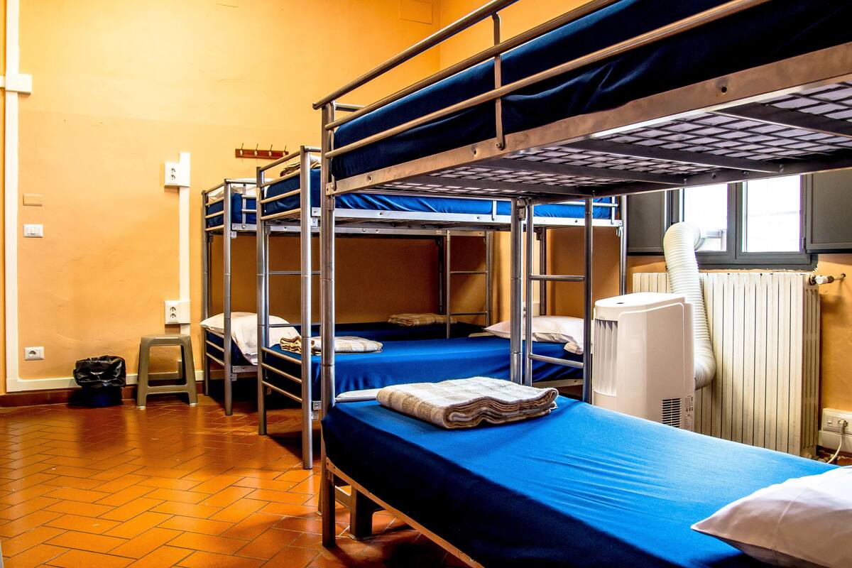 A dormitory room with bunk beds, a radiator, and a window.
