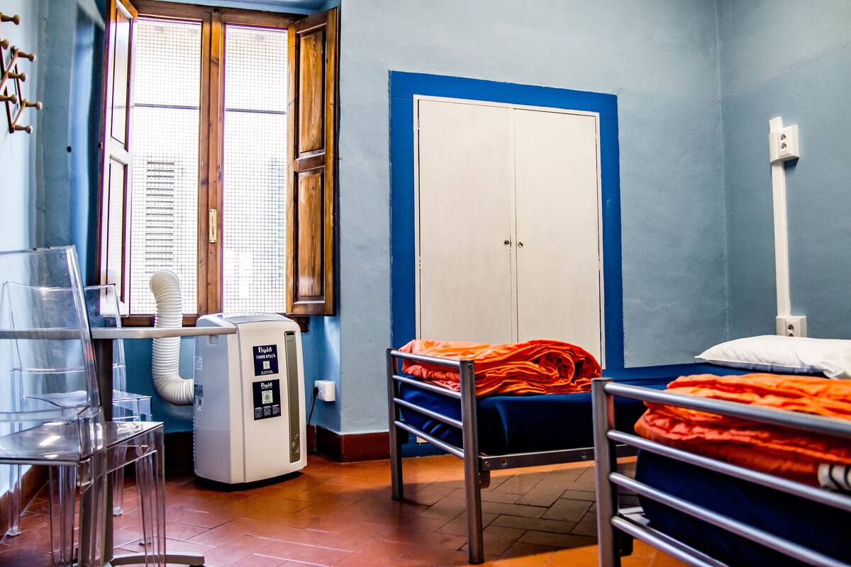 A room with a bed, a wardrobe, a heater, and a window with blinds.