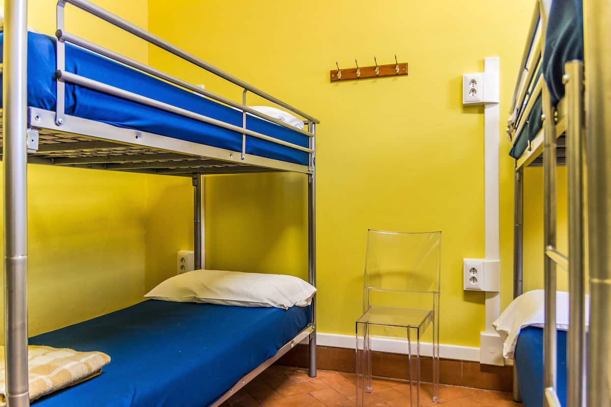 A bunk bed room with a blue mattress, a white pillow, and a clear plastic chair.