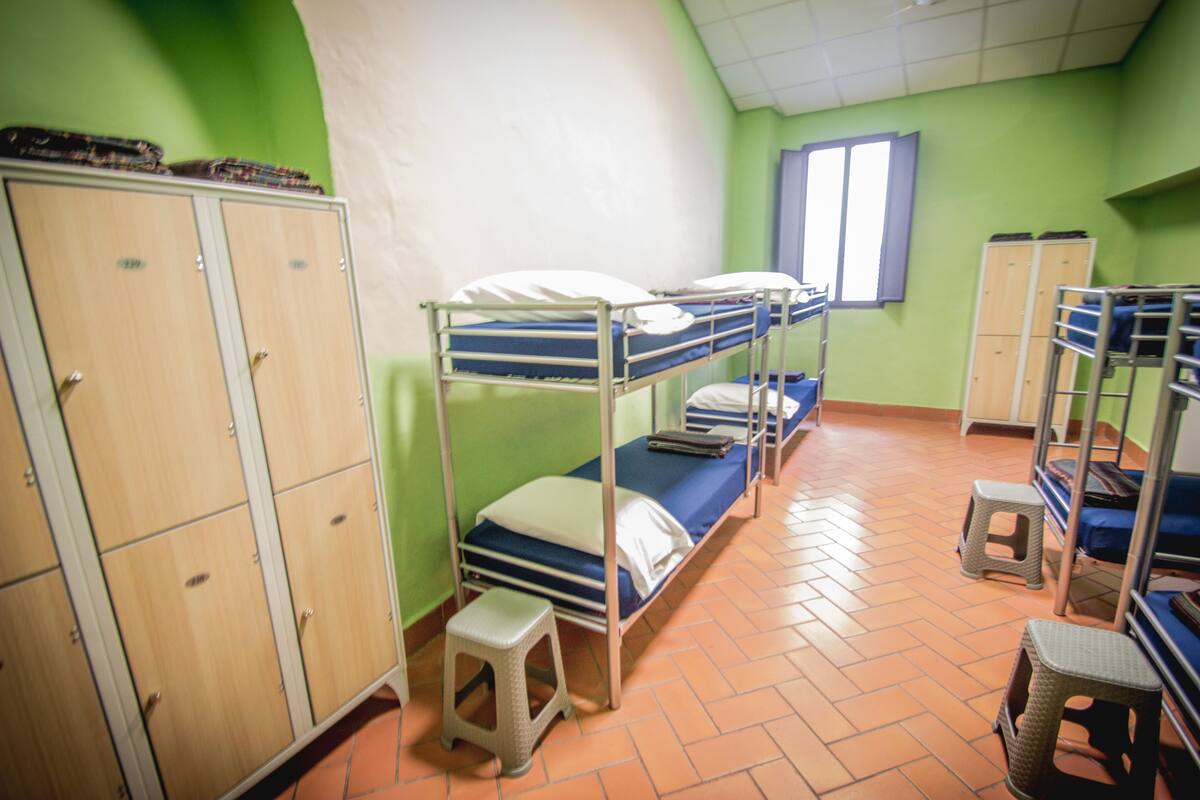 A dormitory room with bunk beds, a wardrobe, and a window.