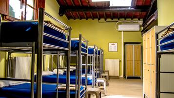 A dormitory room with bunk beds, a radiator, and a wooden wardrobe.