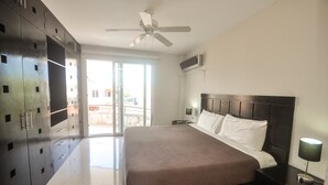Una camera da letto con un letto grande, una ventola a soffitto, un condizionatore d'aria, un comodino e vista dalla finestra.