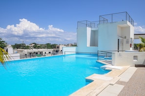 A swimming pool with a clear blue water, a white building with a balcony, and a clear sky with clouds. - Amalfi 201 by Vimex (Playa del Carmen)