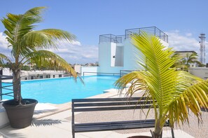 A swimming pool with a blue water feature, surrounded by palm trees and a bench.