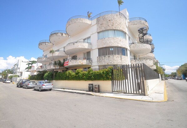 A multi-story building with balconies, a gated entrance, and parked cars along the street.