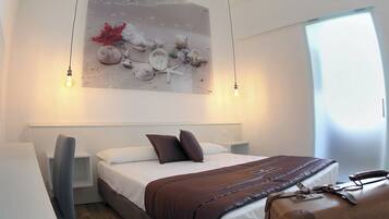 Ein modernes Hotelzimmer mit einem großen Bett, einem Schreibtisch und einem Stuhl. An der Wand hängt ein Gemälde und auf dem Bett liegt ein Koffer.