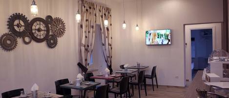 Un comedor con varias mesas y sillas, un televisor montado en la pared y decoración mural.