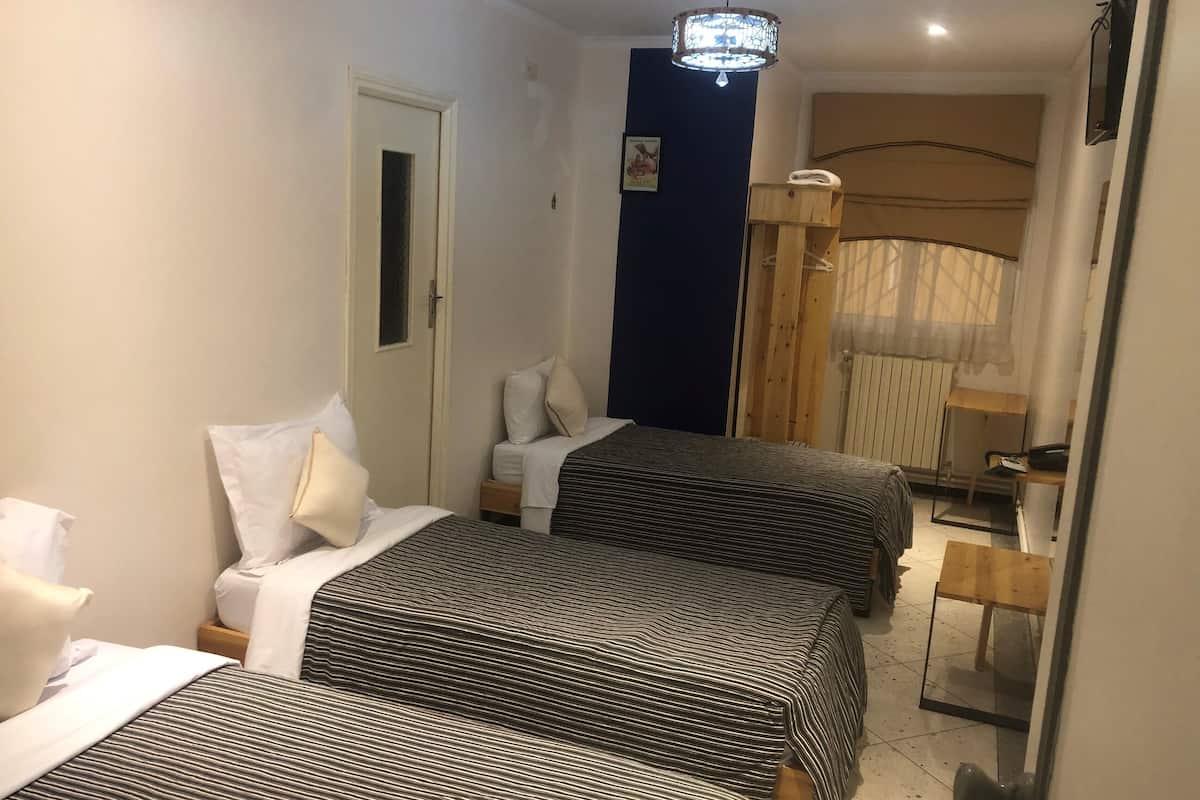Hotellihuone, jossa on kaksi sänkyä, puinen vaatekaappi, peili ja kattovalaisin.