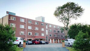 A multi-story hotel with a red facade, a central entrance, and a parking area with several cars. - Seasons Inn Halifax (Halifax)