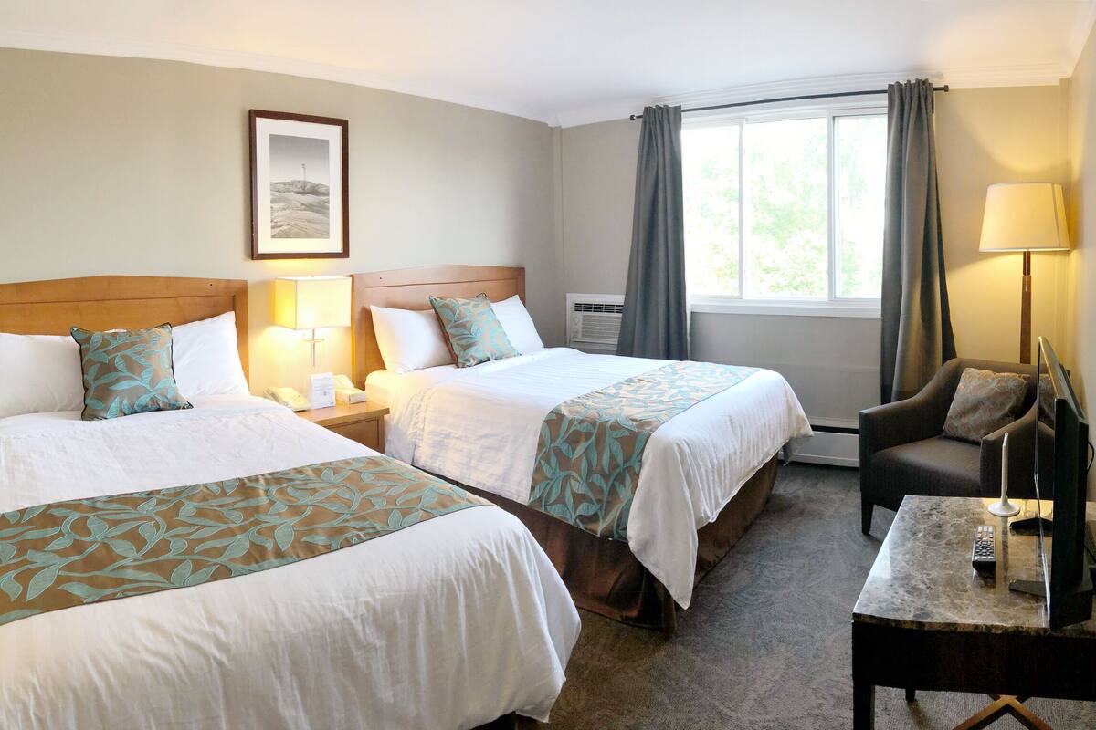 Habitación de hotel con dos camas, un escritorio con lámpara, una silla y una ventana con cortinas.