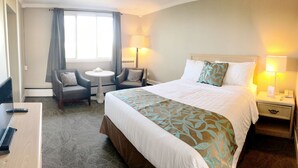 A hotel room with a bed, two armchairs, a small table, a desk, and a nightstand with lamps. - Seasons Inn Halifax (Halifax)