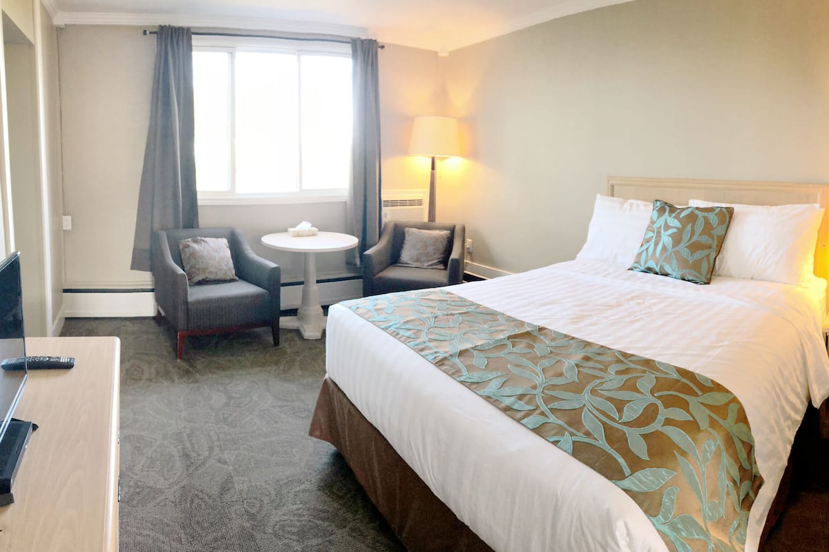 Una habitación de hotel con una cama, dos sillones, una mesita, un escritorio y una mesita de noche con lámparas.