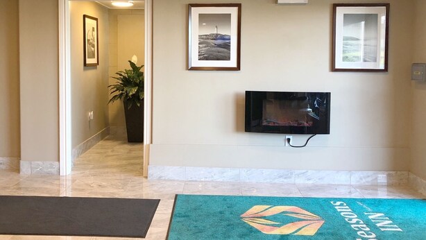 A hotel lobby with a reception desk, a television mounted on the wall, framed pictures on the wall, and a green carpet with a logo. - Seasons Inn Halifax (Halifax)