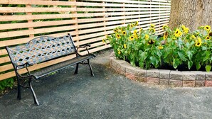 A bench with a metal backrest and black legs, positioned next to a wooden fence and a tree with sunflowers. - Seasons Inn Halifax (Halifax)