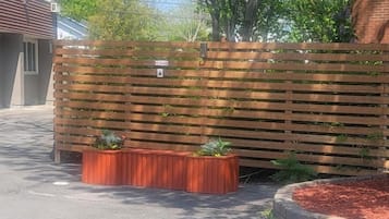 A wooden fence with a small sign, a paved area, and a brick planter with plants.
