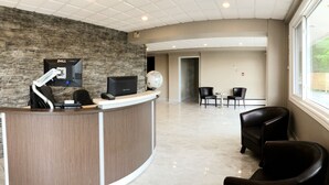 A reception area with a stone wall, a desk with a computer, and a large globe. There are two chairs and a small table in the background. - Seasons Inn Halifax (Halifax)
