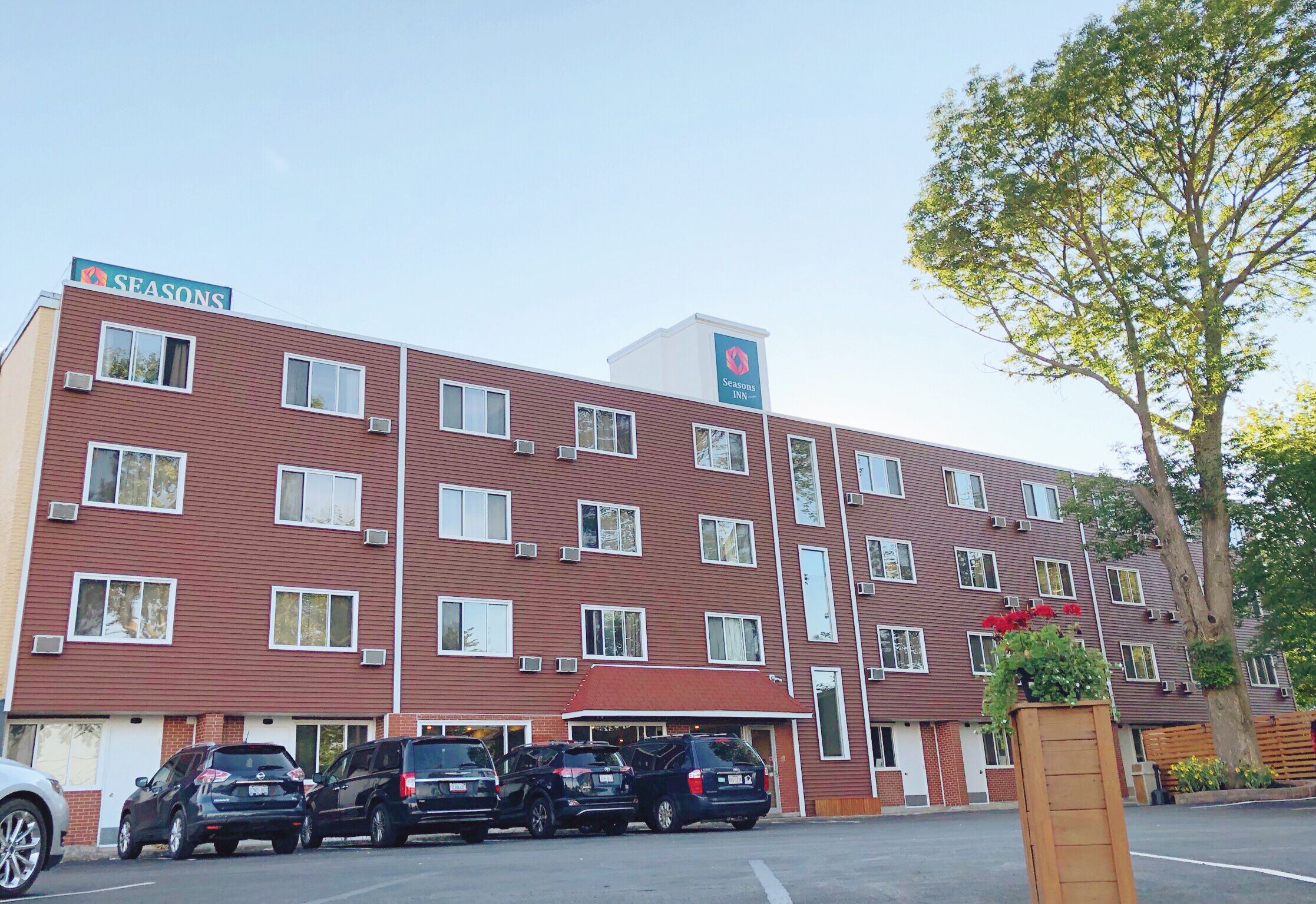 A Seasons Inn building with multiple floors, air conditioning units, and a parking lot with several cars.
