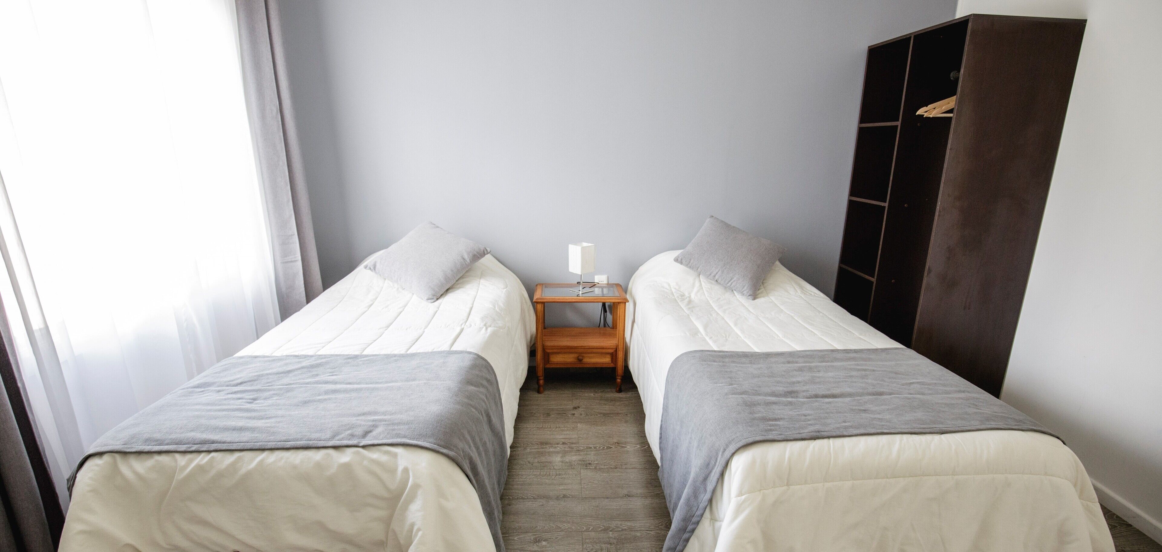 Ein Zimmer mit zwei Einzelbetten, einem Nachttisch mit Lampe und einem Kleiderschrank.