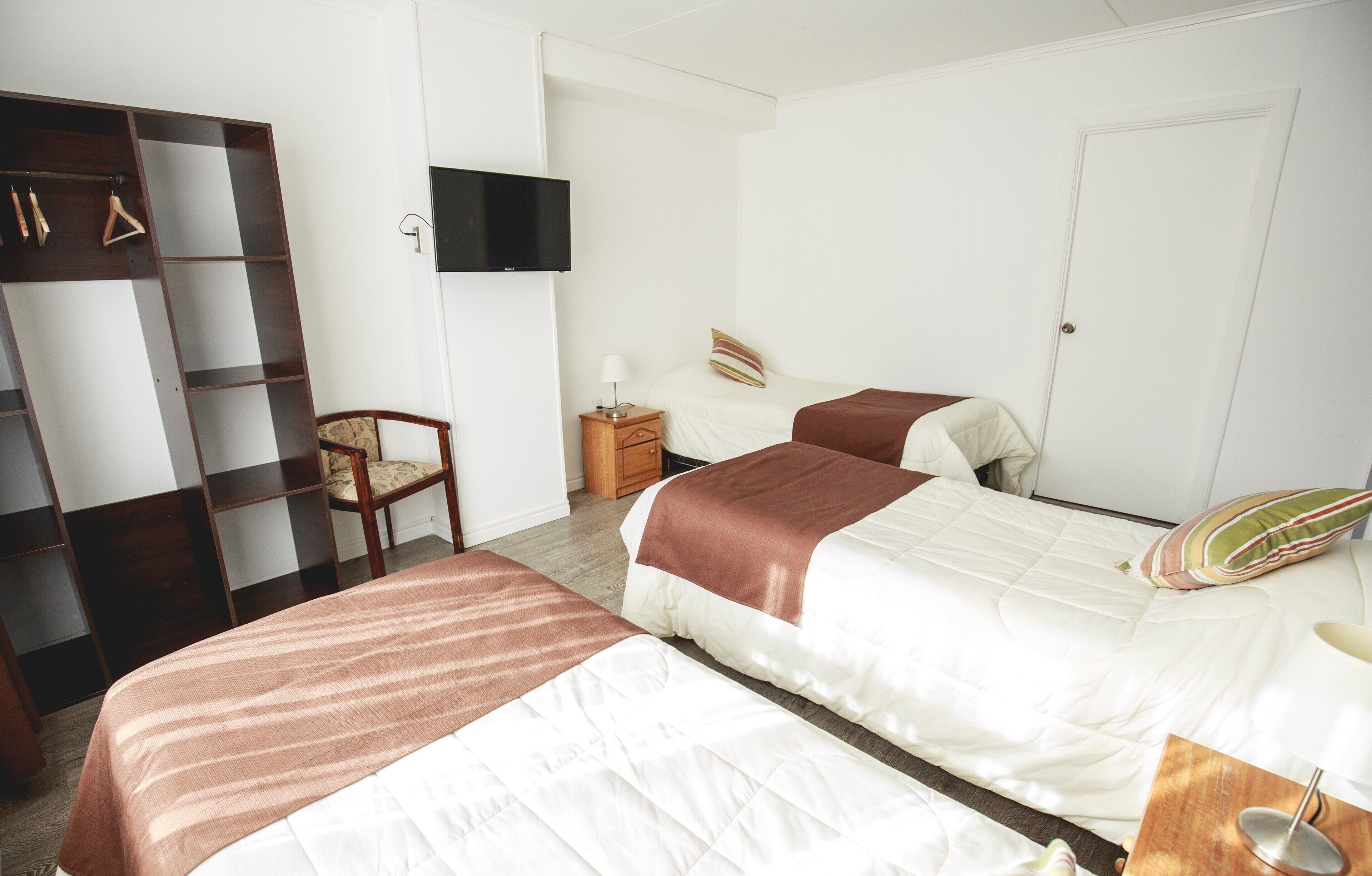 A hotel room with two beds, a wardrobe, a television, and a chair.