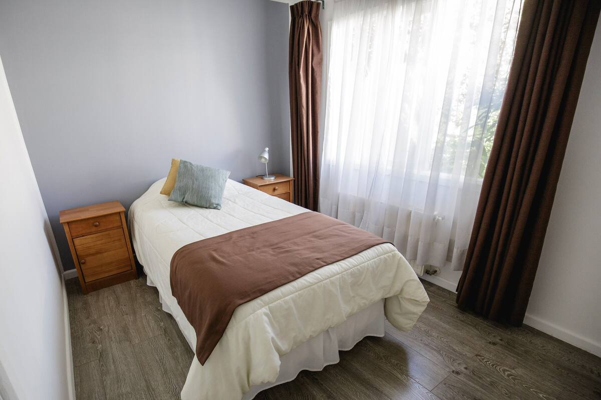 A bedroom with a bed, a nightstand, a lamp, and a window with curtains.