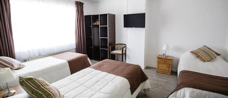 A hotel room with two beds, a wardrobe, a chair, a TV, and a bedside table with a lamp.
