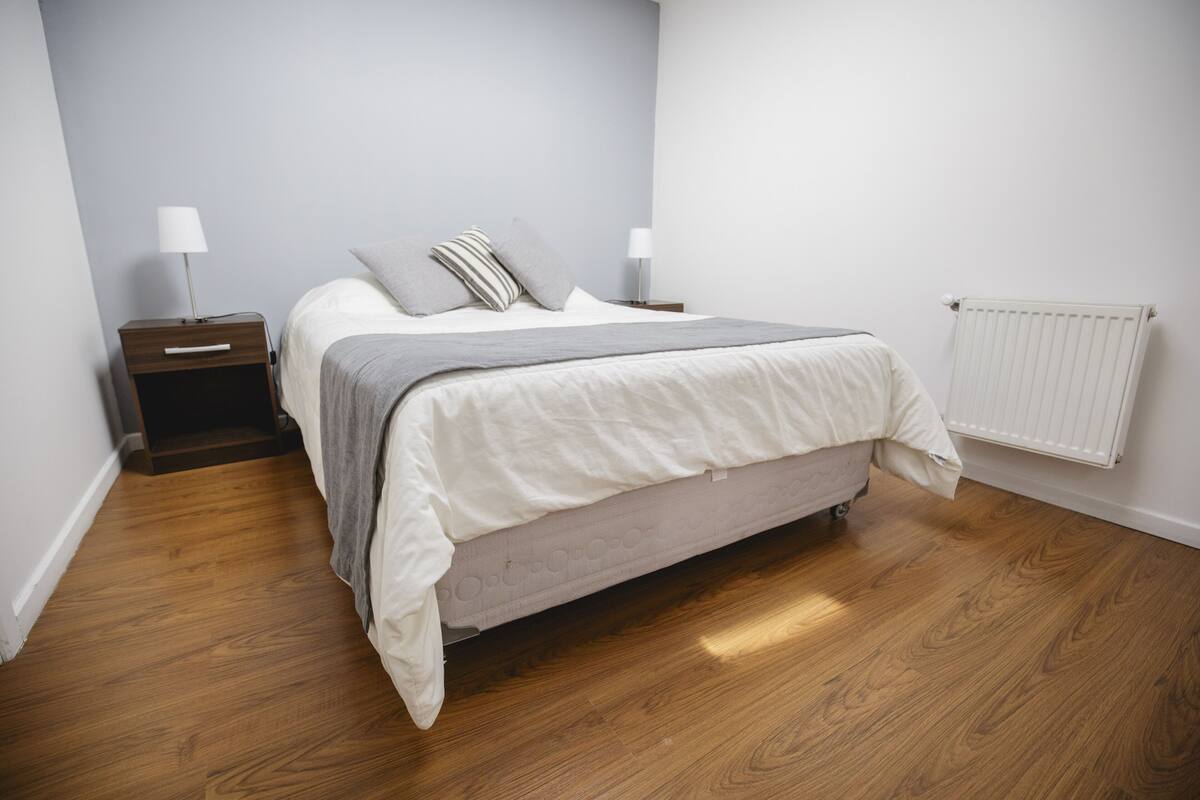 A bedroom with a bed, nightstands, a radiator, and wooden flooring.