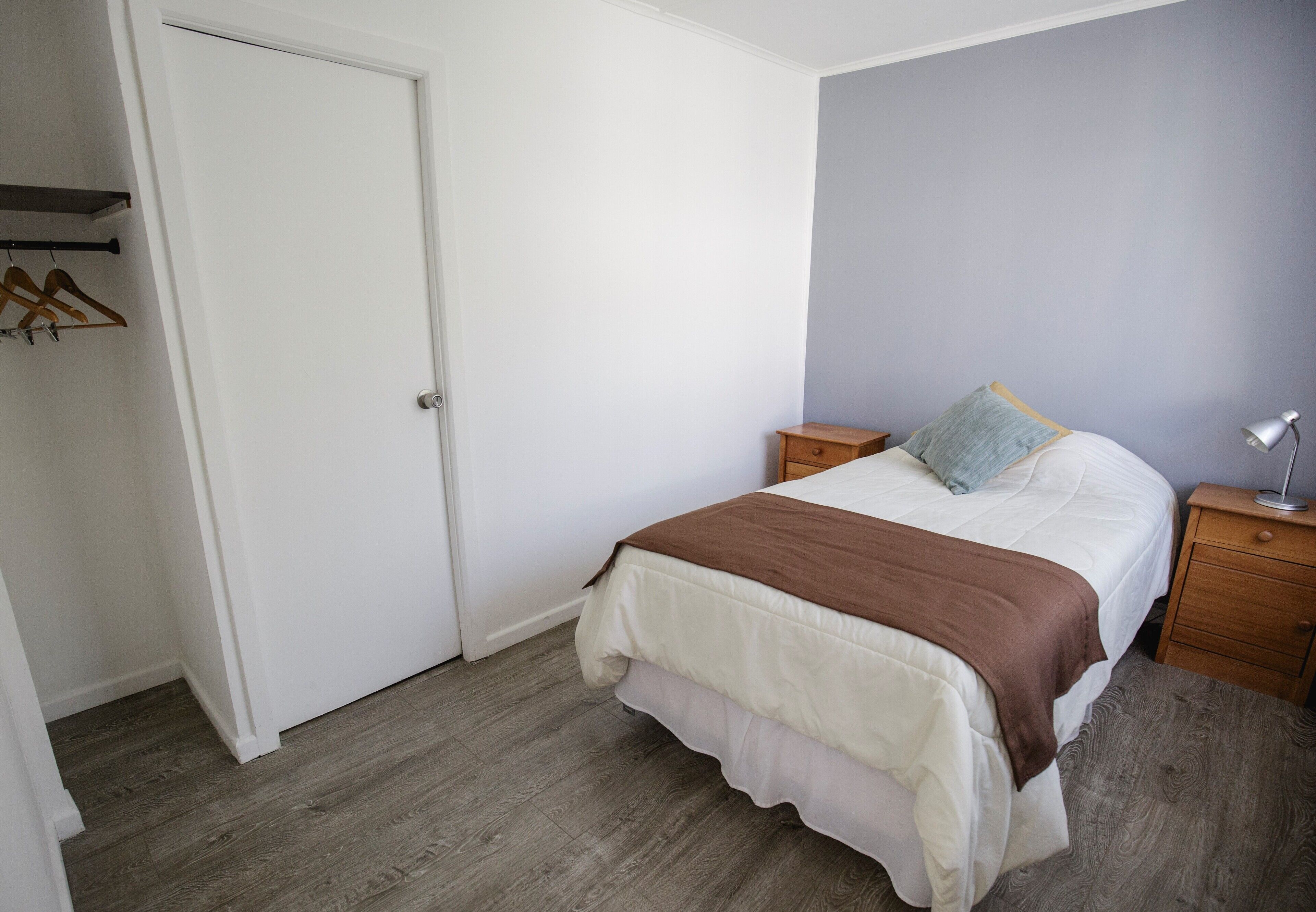 Een slaapkamer met een bed, nachtkastje, houten dressoir en een deur.
