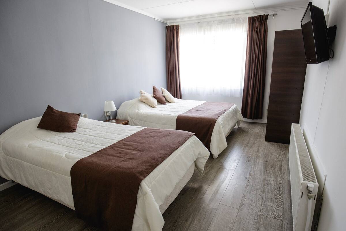 A hotel room with two beds, a TV mounted on the wall, and a window with curtains.