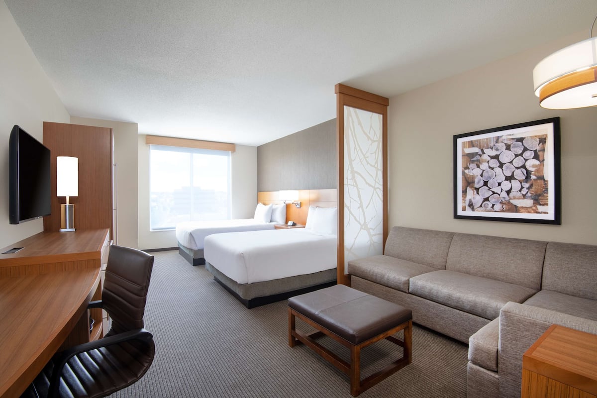A hotel room with a wooden desk, two beds, a sofa, and a television.