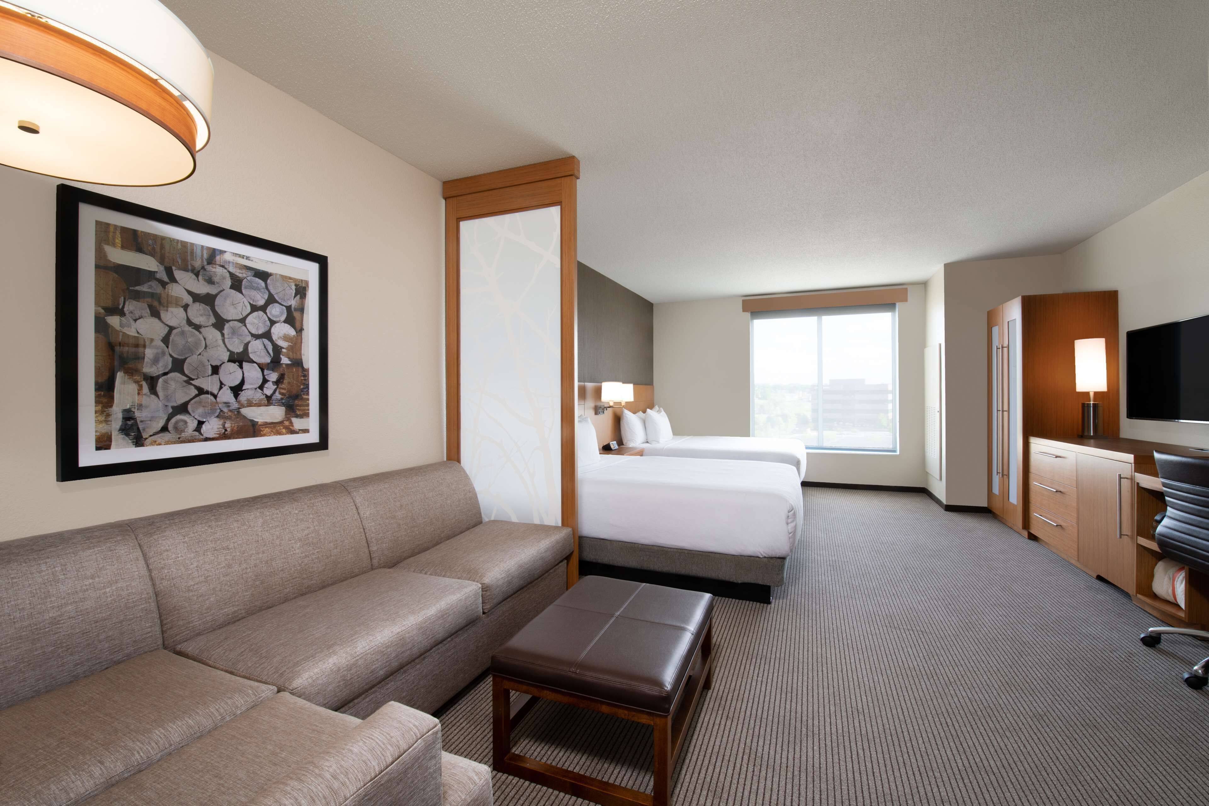 A hotel room with a sofa, a small table, a bed, a TV, and a large window.