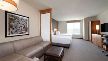 A hotel room with a sofa, a small table, a bed, a TV, and a large window.