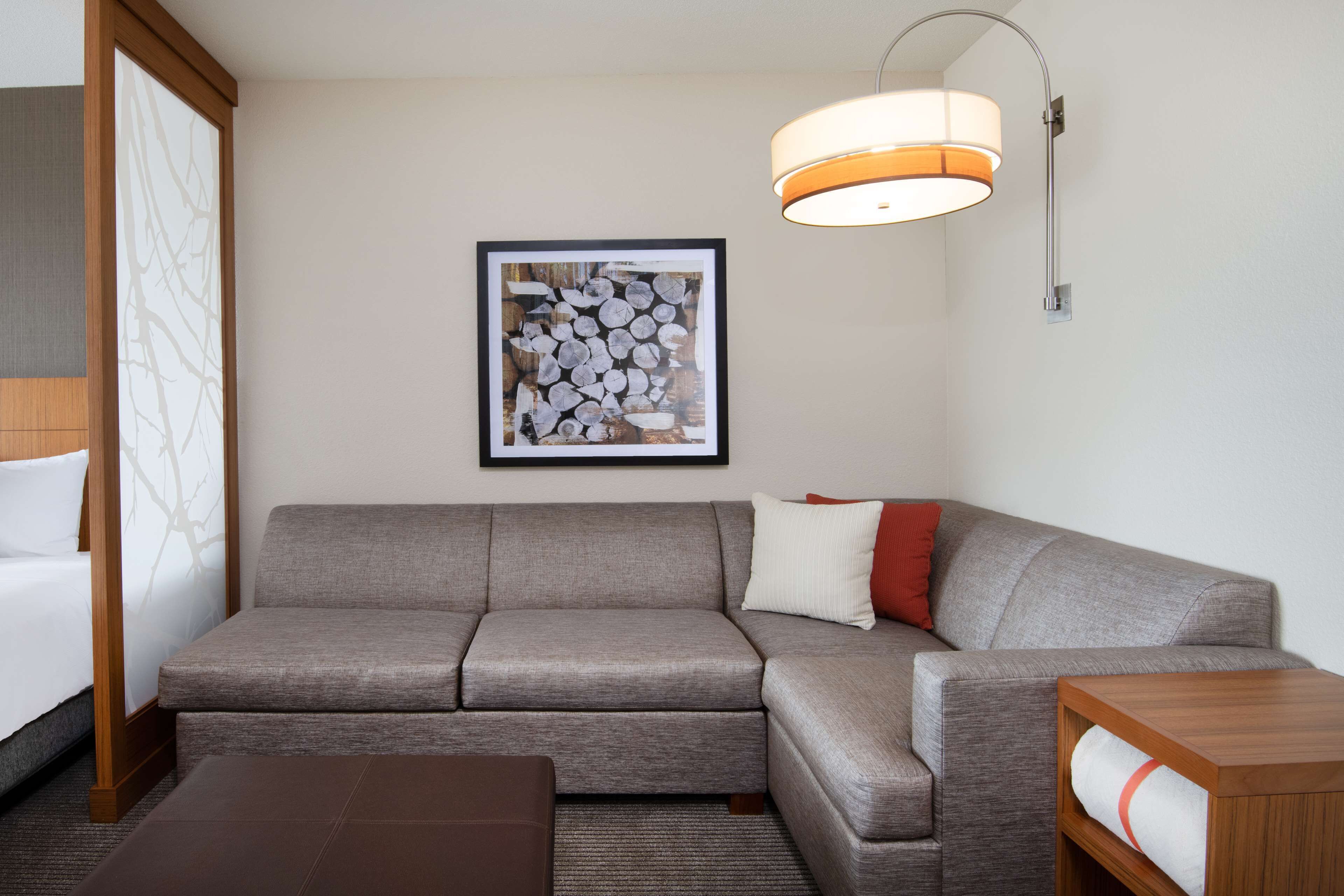 A modern hotel room with a grey sofa, a wooden coffee table, and a framed artwork on the wall.