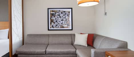 A modern hotel room with a grey sofa, a wooden coffee table, and a framed artwork on the wall.