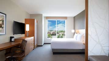 A hotel room with a bed, a desk with a chair, a TV, and a window with a city view.