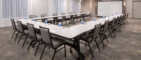 A conference room with a long table, chairs, water bottles, and a projector screen.