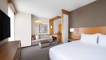 A hotel room with a large bed, a desk, a sofa, and a TV.