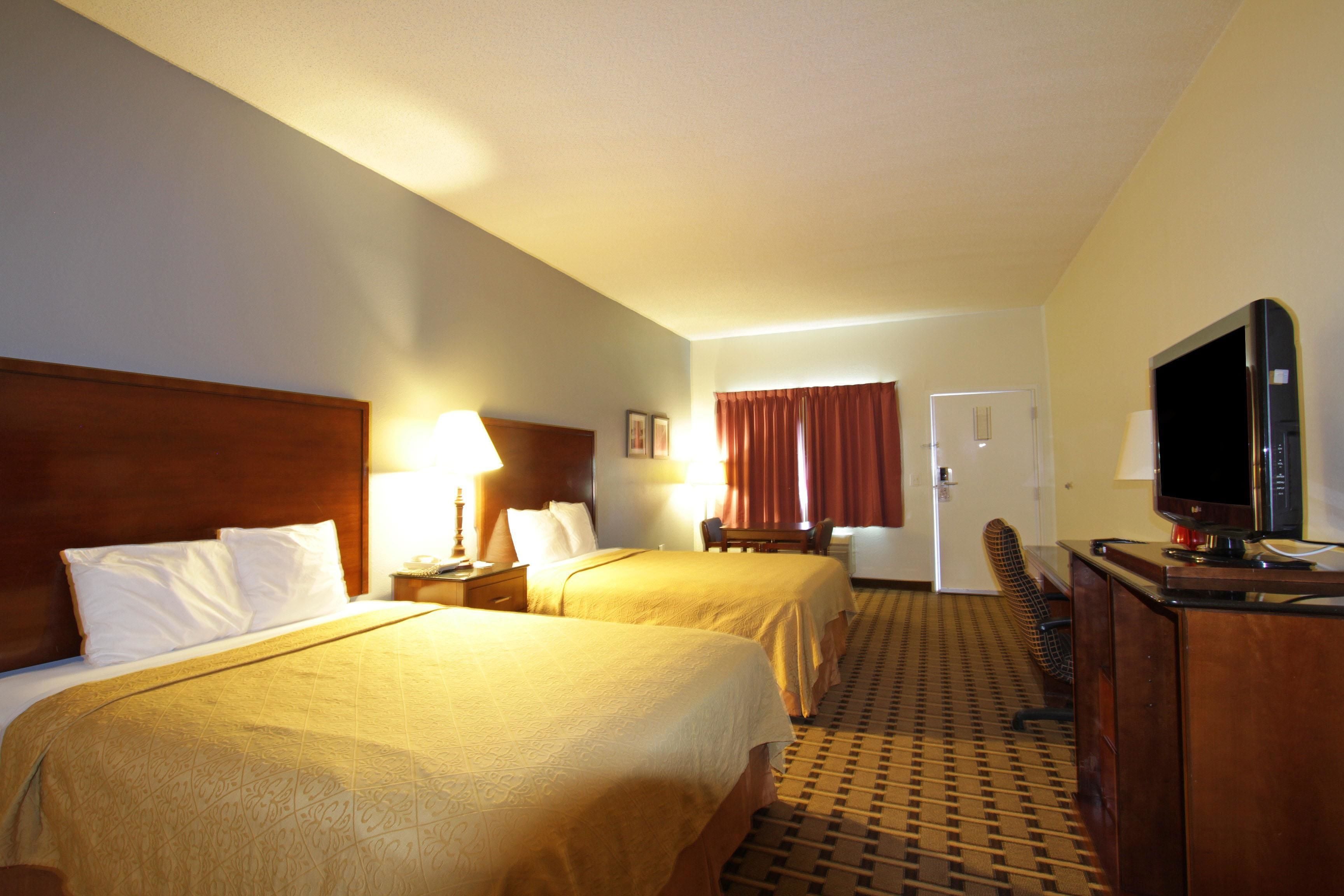 A hotel room with two beds, a desk with a television, a chair, and a desk lamp.