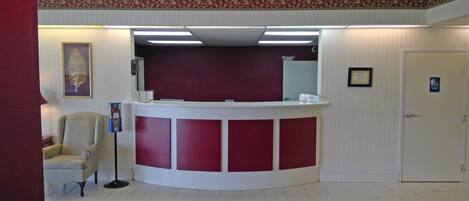 A reception area with a curved desk, a chair, a framed picture on the wall, and a door with a wheelchair accessibility sign.
