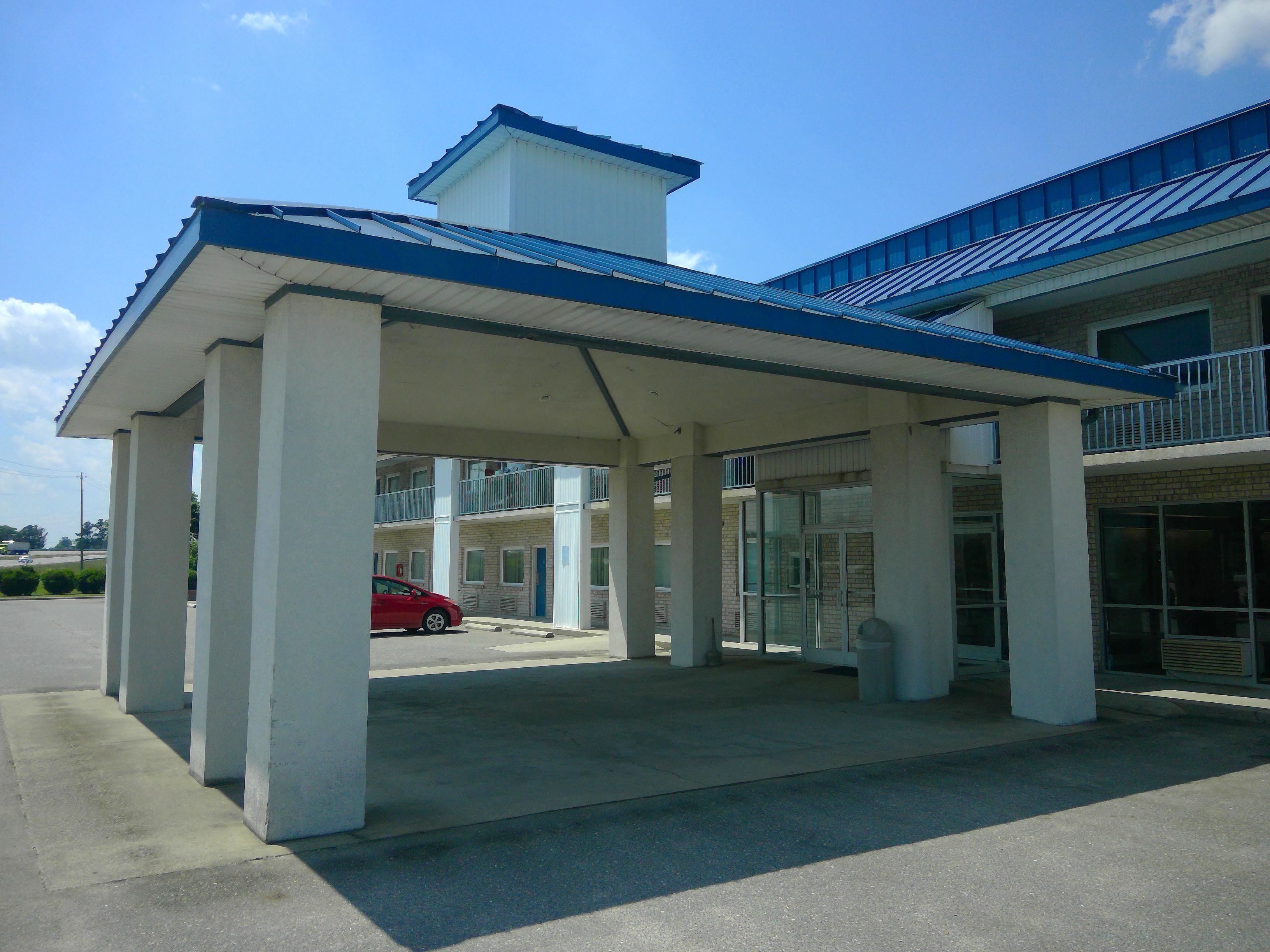 A building with a covered entrance, columns, and a red car parked outside.