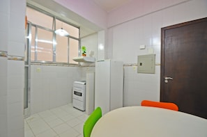 A kitchen with white tiled walls, a white refrigerator, a stove, and a window with blinds. There is a green chair and an orange chair at a table. - LineRio Copacabana Family Residence 322 (Rio de Janeiro)