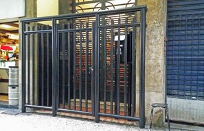 A metal gate with vertical bars, a small stool, and a closed shutter door in the background. - LineRio Copacabana Family Residence 322 (Rio de Janeiro)