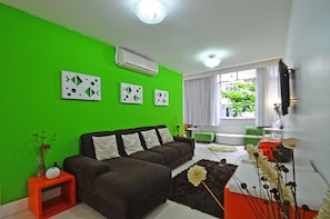 A modern living room with a green wall, a brown sofa, a small orange side table, and a white vase with flowers. - LineRio Copacabana Family Residence 322 (Rio de Janeiro)
