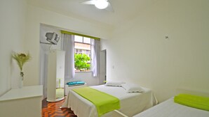Ein Hotelzimmer mit zwei Betten, einem Deckenventilator, einem Fenster mit Vorhängen und Blick auf einen grünen Baum.
