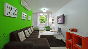 Ein modernes Wohnzimmer mit grüner Wand, einem braunen Sofagarnitur, einem Flachbildfernseher und einer roten Unterhaltungseinheit.