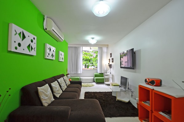 A modern living room with a green wall, a brown sofa set, a flat-screen TV, and a red entertainment unit. - LineRio Copacabana Family Residence 322 (Rio de Janeiro)