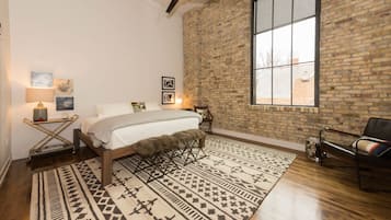 Un dormitorio con un ventanal grande, una cama con una manta de piel sintética, un tapete estampado y una pared de ladrillo.