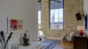 A modern living room with a large window, a white console table, a blue patterned rug, and a red lamp. - Kinn Guesthouse Bay View (Milwaukee)