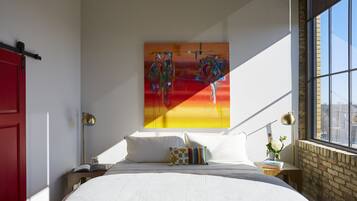 Un dormitorio con una cama grande, una puerta roja, un cuadro en la pared y una ventana con vistas.
