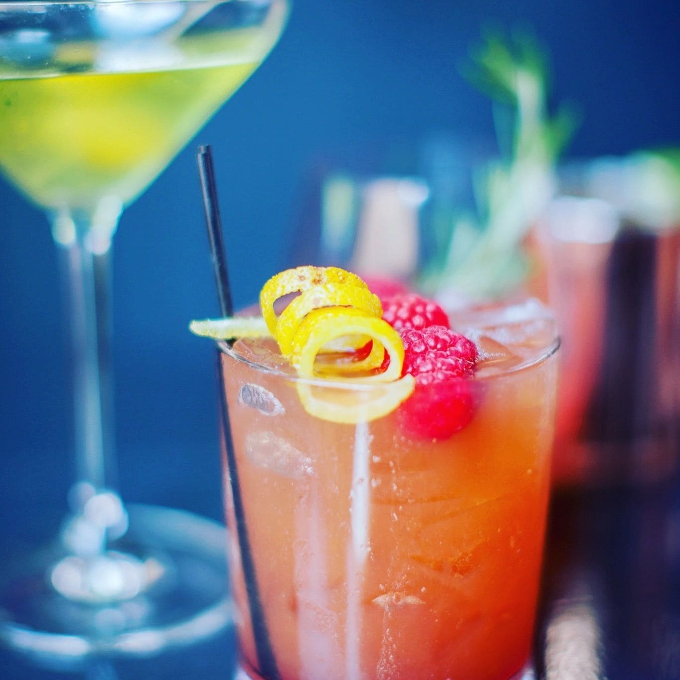 Un cocktail dans un verre, garni d’une tranche de citron et de framboises.